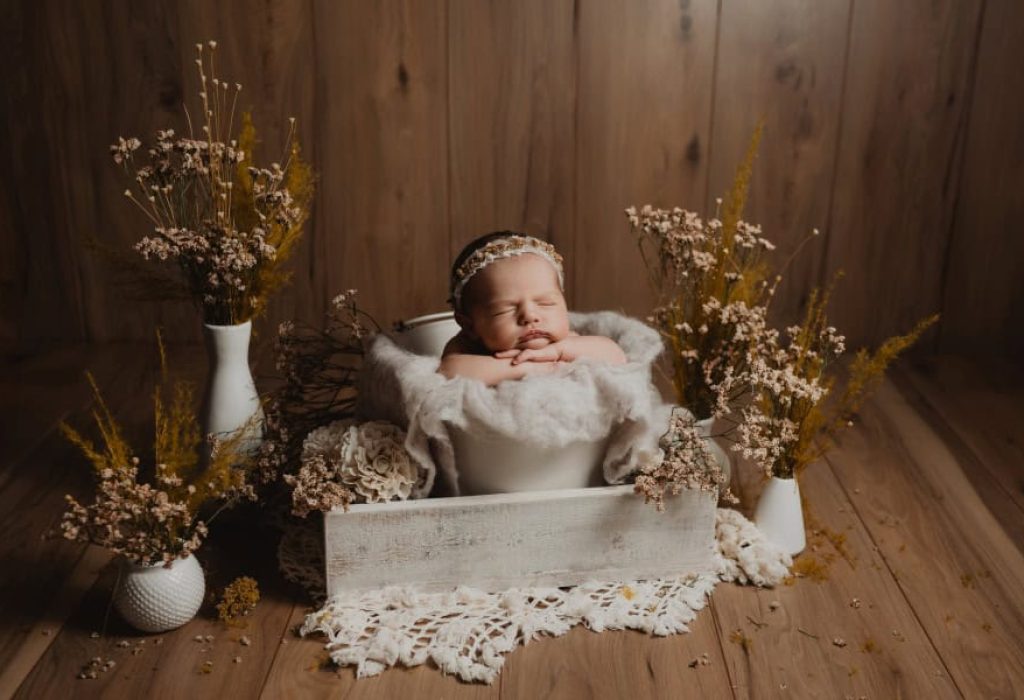 Newborn baby in white bucket with neutral floral styling and wood wall backdrop in NH studio