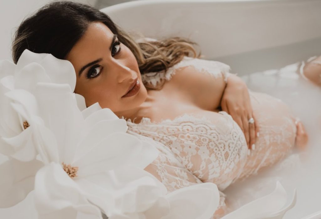 Maternity milk bath session with floral accents and a pregnant woman peacefully resting in tub, photographed in natural light studio
